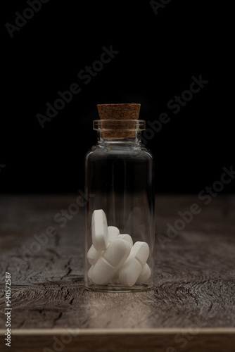 Pills in the glass phial on the dark background