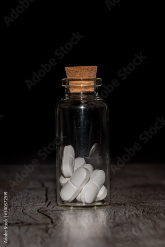 Pills in the glass phial on the dark background