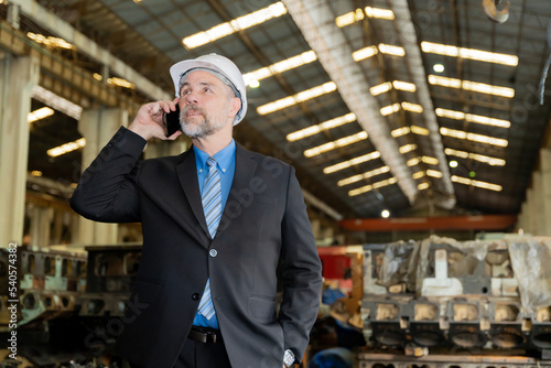 A businessman checks on-site maintenance work at an old factory for train rehearsals. talking on the phone with customers or employees