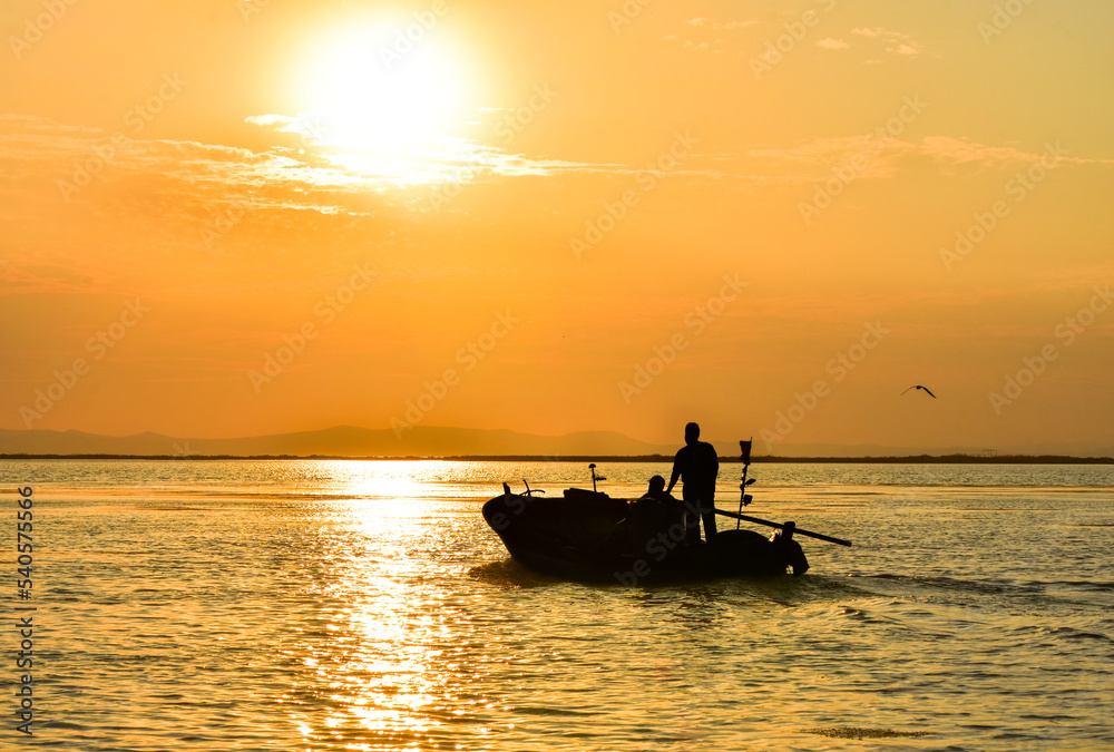Fisherman and fishing boat silhouette on a sea at sunset.