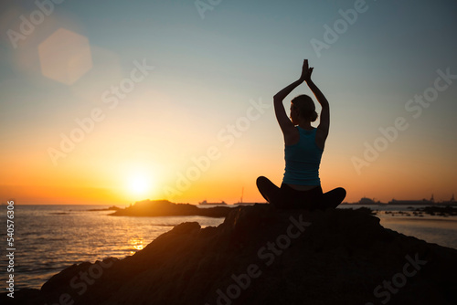 Yoga woman silhouette, meditating on the ocean beach during a beautiful sunset.