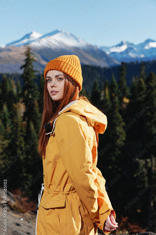 Woman in yellow raincoat hiking stands in front of mountains in yellow cap autumn sunset light Woman in yellow raincoat hiking stands in front of mountains in yellow cap autumn sunset light