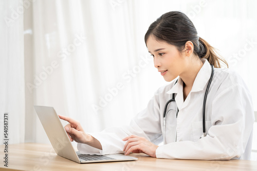 Asian female doctor using laptop computer online video call remote talking to patient. Medical practitioner giving online virtual consultation to patient from hospital office.