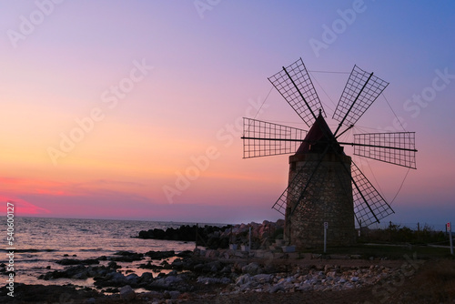 Windmill on the shore seaside with sunset in the background. North of Sicily, Trapani, old fashioned windmill on the coast