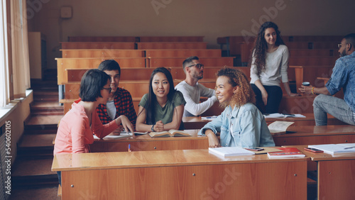 Multiracial group of university students are relaxing and chatting during break enjoying free time and communication. Wooden tables, attractive people and noteboks are visible. photo