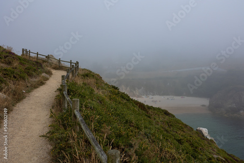 The path for hiking is high above the ground  you can see the beach with sand and blue water  the bay. Heavy fog poor visibility.