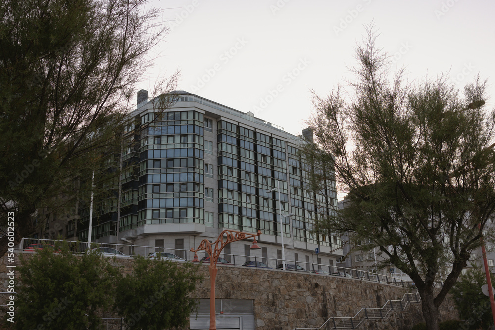 The facade of a stylish modern building, a residential building, is surrounded by trees with green branches. The facade of a stylish modern building, a residential building, is surrounded by trees with green branches.