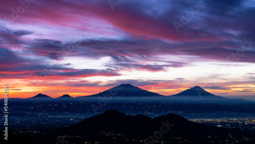 A beautiful colorful epic sunrise sky with mountain range and beautiful city lights - Magelang City and Merapi  Merbabu  Andong  Telomoyo mountain looking out from slope of Mount Sumbing