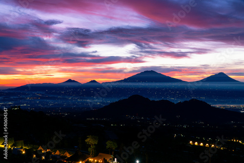 A beautiful colorful epic sunrise sky with mountain range and beautiful city lights - Magelang City and Merapi, Merbabu, Andong, Telomoyo mountain looking out from slope of Mount Sumbing photo