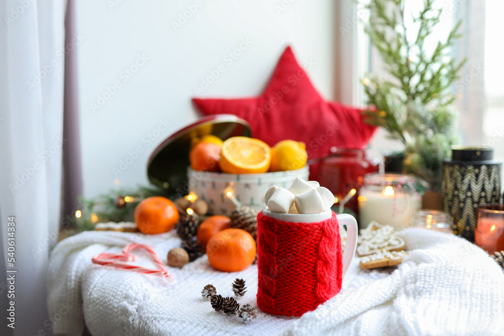 A cup of cocoa with marshmallows in a red knitted decoration in a New Year's interior