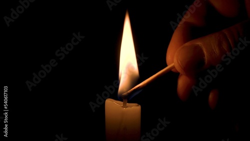 A Male Hand Lights a Wax Candle with a Match on a Black Background. Bright Flame, Glowing Fire, Ignition in the Darkness. Concept of Memory, Ritual, Remembrance, Celebration or Religious Ceremony