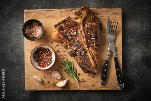 Grilled T-Bone Steak with salt and pepper  on cutting board on dark grey background. Roasted T-Bone beef steak. photo