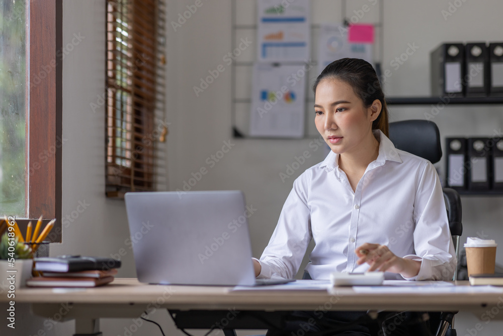 Business Asian woman using calculator and laptop for doing math finance on an office desk, tax, report, accounting, statistics, and analytical research concept Business Asian woman using calculator and laptop for doing math finance on an office desk, tax, report, accounting, statistics, and analytical research concept