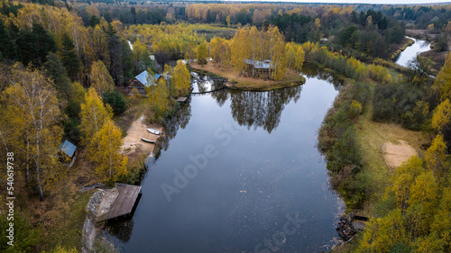 Fototapeta Naklejka Na Ścianę i Meble -  panoramic view from a drone on the edge of the forest with wooden houses and a river against the backdrop of autumn nature