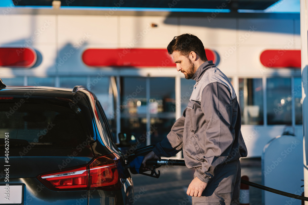 A gas station worker holds a petrol dispenser and fills up the car tank. A gas station worker holds a petrol dispenser and fills up the car tank.