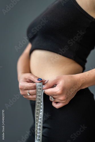 waist view of a sporty woman measuring her size with a tape.