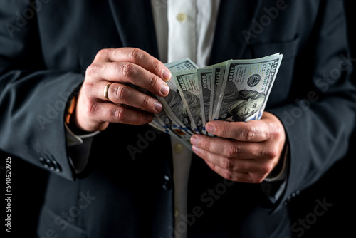 man in a stylish suit is counting his savings in dollar bills.