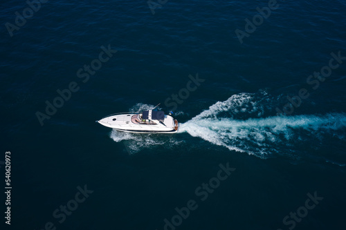 White yacht moves on dark water aerial view. Big white boat with blue awning moving on the water aerial view.