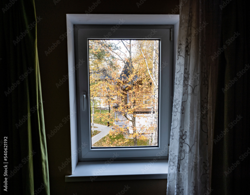 autumn landscape with yellow trees against the background of wooden houses in the window frame from the room autumn landscape with yellow trees against the background of wooden houses in the window frame from the room