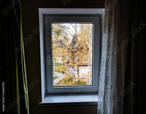 autumn landscape with yellow trees against the background of wooden houses in the window frame from the room