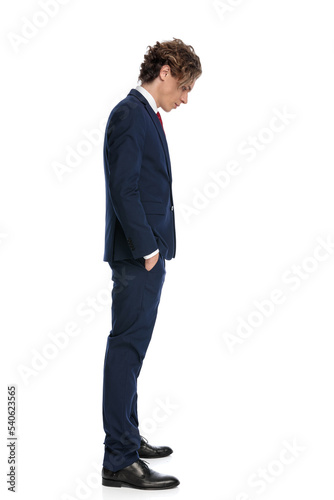 attractive young businessman with hands in pockets looking down