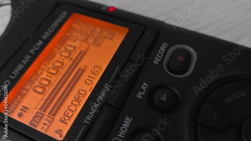 Finger presses record button of digital voice audio dictophone during interview or interrogation. Screen with wave form of speech recording of journalist. Electronic portable device for media reporter