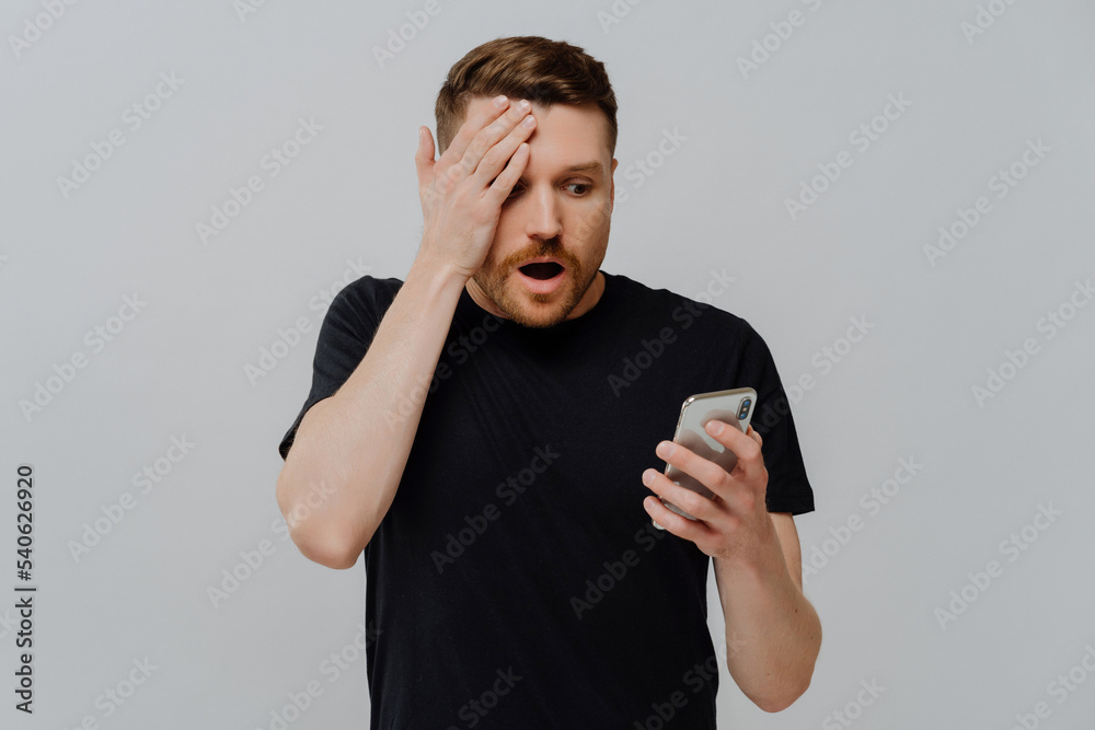 Impressed guy reading unexpected news in social media on smartphone with amazed expression Impressed guy reading unexpected news in social media on smartphone with amazed expression