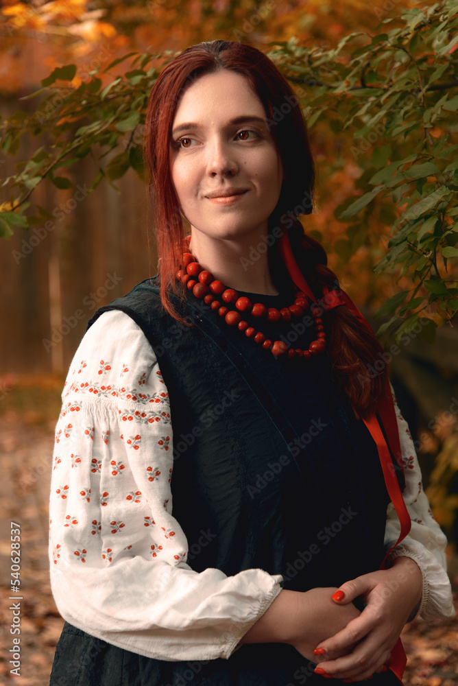 Smiling young redhead woman dressed traditional ukrainian embroidered clothes and red beads looking away. Vintage outfit. Half-length portrait.