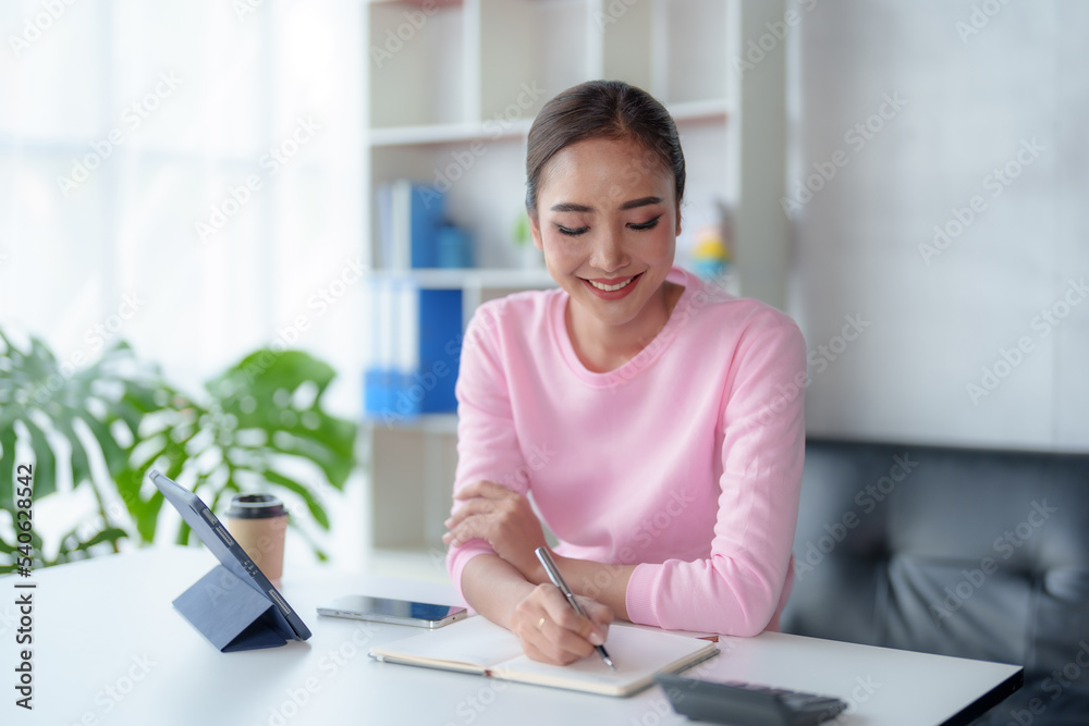 Obraz premium Beautiful American women student studying online takes notes on her laptop to gather information about her work smiling face and a happy study posture.