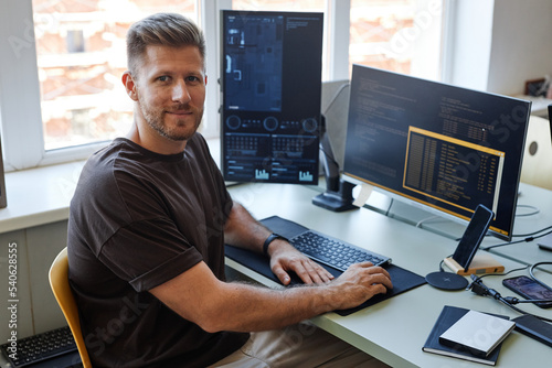 Obraz w ramie Portrait of young software engineer looking at camera while writing code at workplace with multiple computer screens