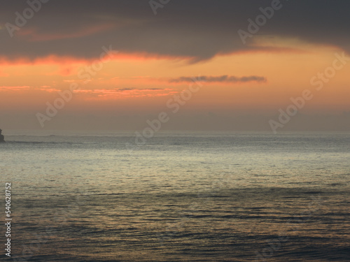 Peaceful sunrise over the ocean with small waves and clouds