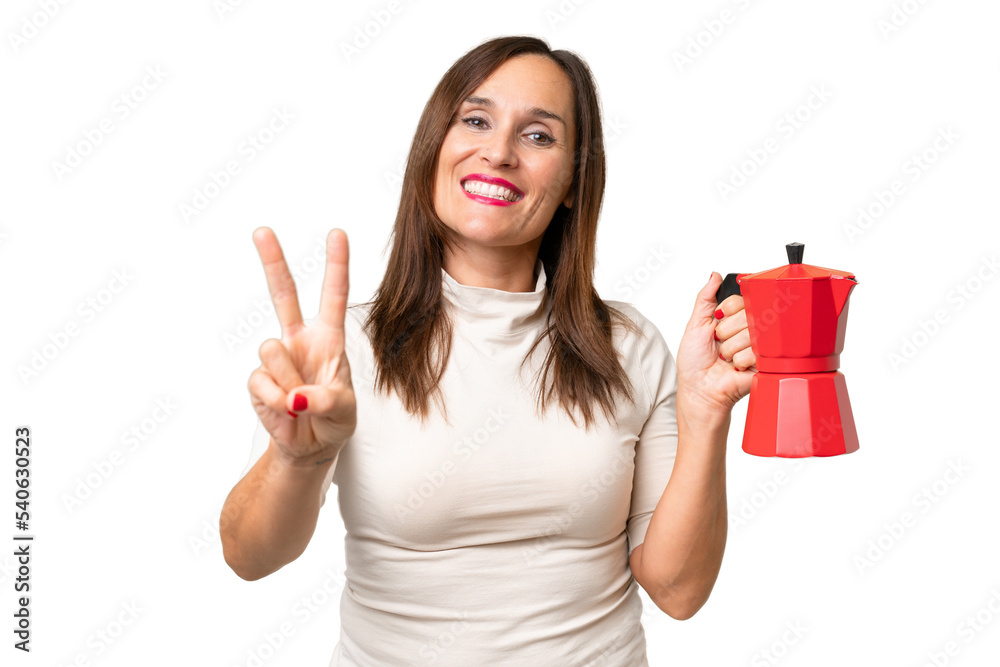 Middle-aged caucasian woman holding coffee pot over isolated background smiling and showing victory sign Middle-aged caucasian woman holding coffee pot over isolated background smiling and showing victory sign