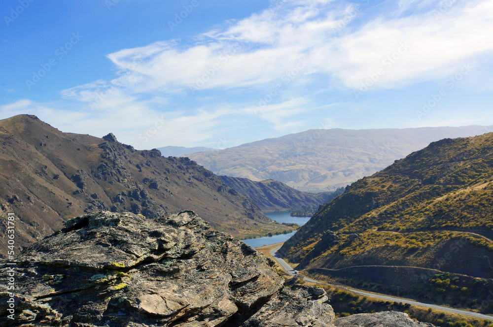 Fototapeta premium View of the Cromwell Gorge and Lake Dunstan from high up on the cycling track on a blue sky Autumn day. Shist rocks in foreground.