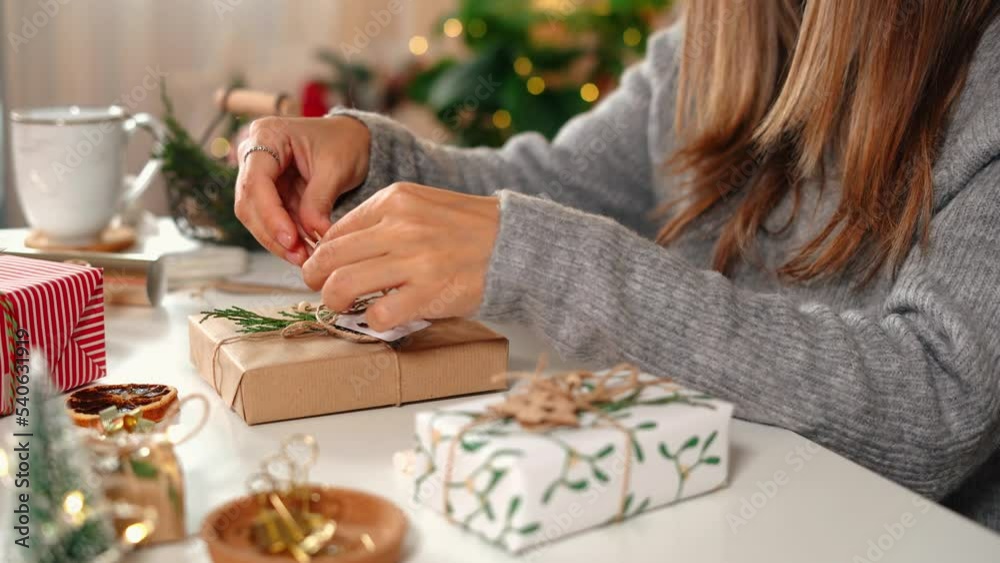 Woman s hands wrapping Christmas gift boxes, close up. Unprepared presents on white table with decor elements and items Christmas or New year DIY packing Concept.