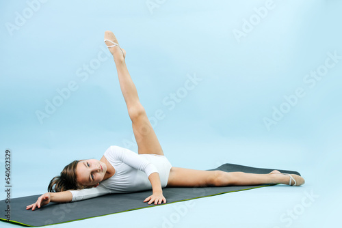 Calm girl in a white leotard lying on a yoga mat, extending straight leg up