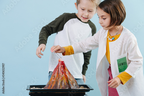 Curious girl in white robes doing chemical volcano experiment with a boy