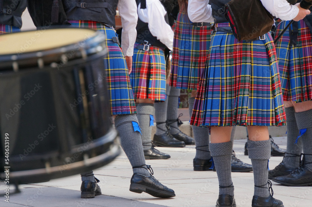 Red and blue tartan kilts and grey socks, flashes and brogues of a Highland Pipe Band practising