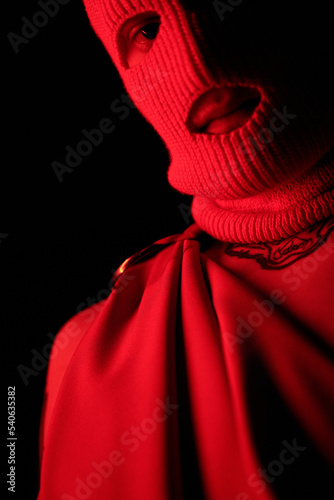 Close-up of young gangster in balaclava standing in dark against black background photo