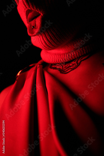 Close-up of man in balaclava with showing piercing in his tongue posing in dark studio photo