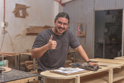 A business owner of a furniture making workshop giving a thumbs up of approval.
