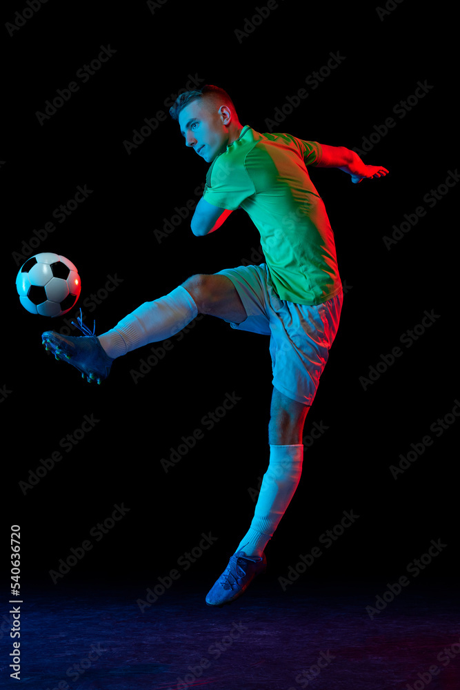 Goal. Young soccer, football player in motion and action with ball isolated on dark background in neon light. Concept of achievement, creativity, sport, energy, championship