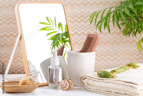 Fototapeta Naklejka Na Ścianę i Meble -  Spa composition in a light  bathroom with towels, oil bottle, cosmetics, Jade roller for face massage, comb and mirror. Morning skin-care routine, summer, tropical plant.