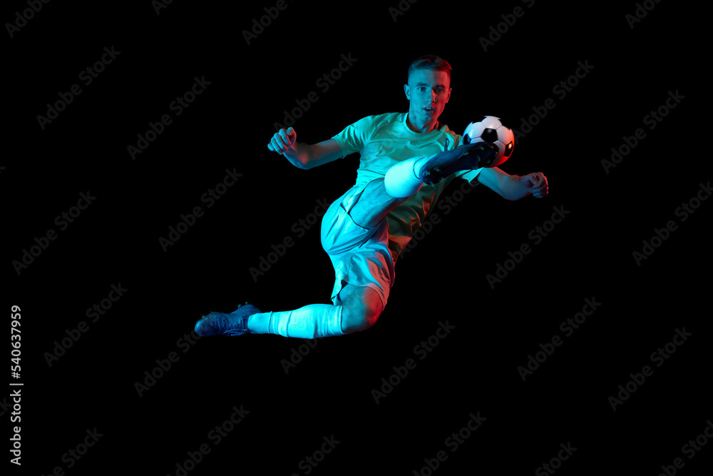 Dynamic shot of young active football player in action isolated on dark background in neon light. Concept of sport, goals, competition, achievements.