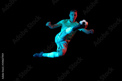 Dynamic shot of young active football player in action isolated on dark background in neon light. Concept of sport, goals, competition, achievements.