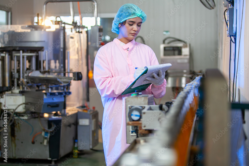 Asian woman worker with clipboard is checking product bottles of fruit juice on the production line in the beverage factory. Manufacturer checks quality of food industry. Asian woman worker with clipboard is checking product bottles of fruit juice on the production line in the beverage factory. Manufacturer checks quality of food industry.