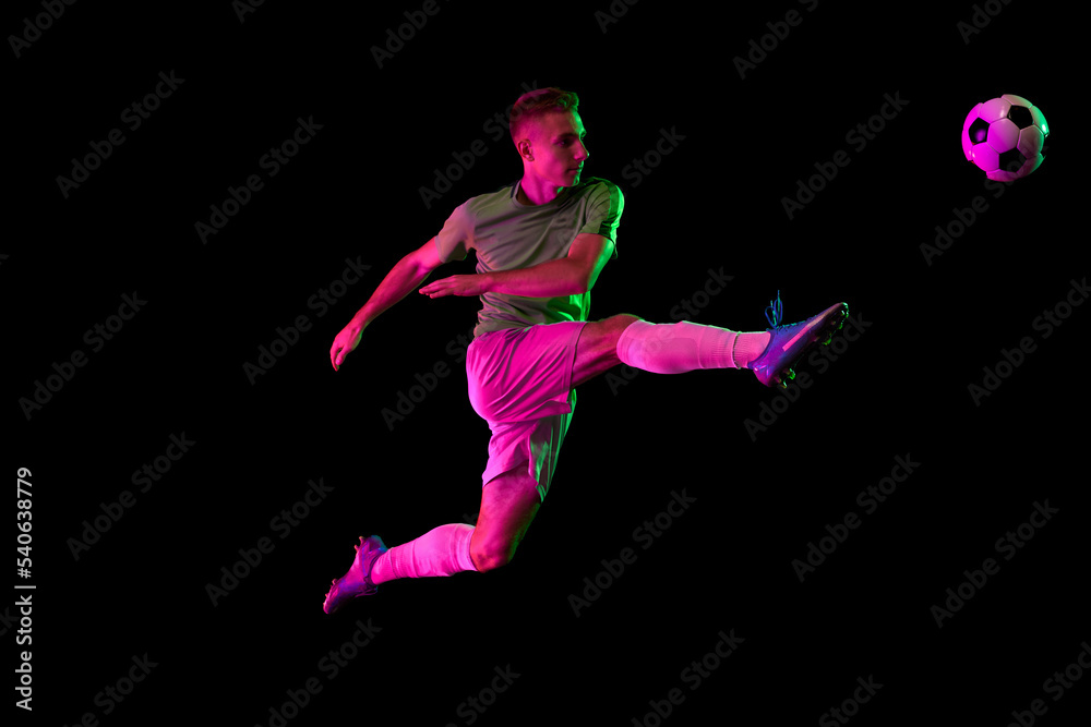 Young professional male football soccer player in motion isolated on dark background in neon light. Concept of sport, goals, competition, league, ad. Young professional male football soccer player in motion isolated on dark background in neon light. Concept of sport, goals, competition, league, ad.