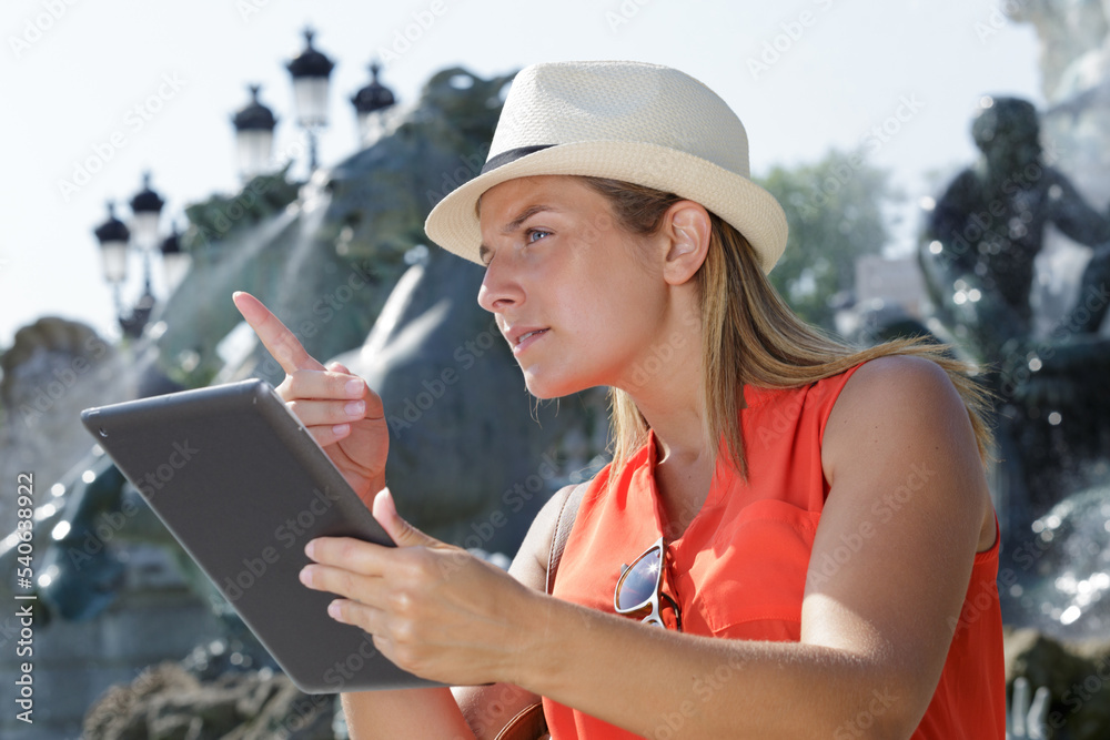Fototapeta premium female tourist holding a tablet in front of fountain