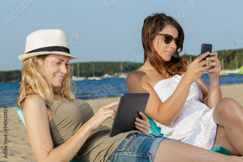 women use touchpad tablet technology on the beach