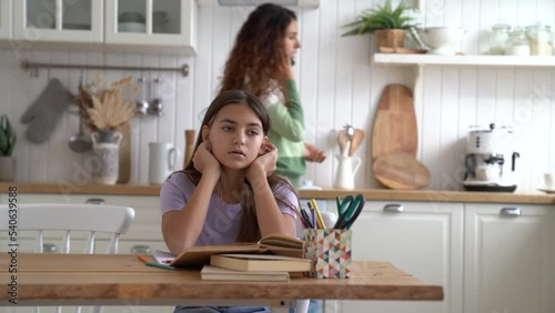 Unfortunate teen girl is sad listening to mother talking to father on phone sits at table in kitchen. Caucasian woman is nervous discussing something making call to teacher or principal of school photo