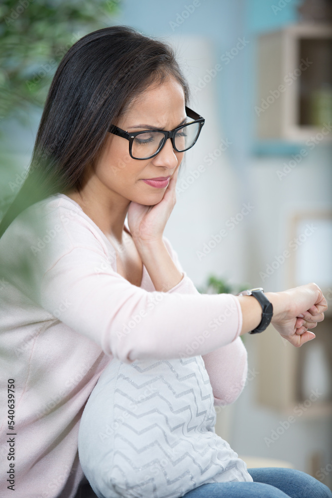 woman at home suffering from toothache looking at wristwatch